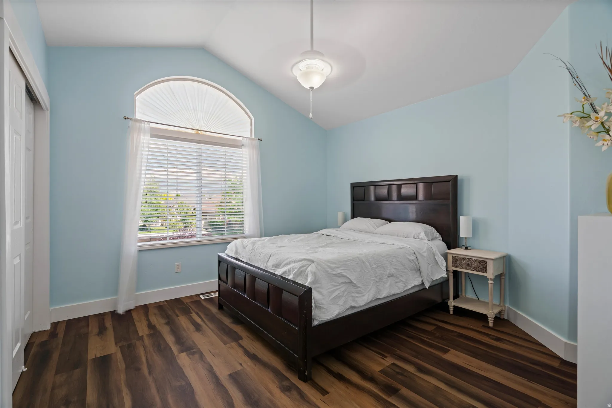 Bedroom featuring a vaulted ceiling with a fan, wood-finish flooring, and a large window with an arched transom