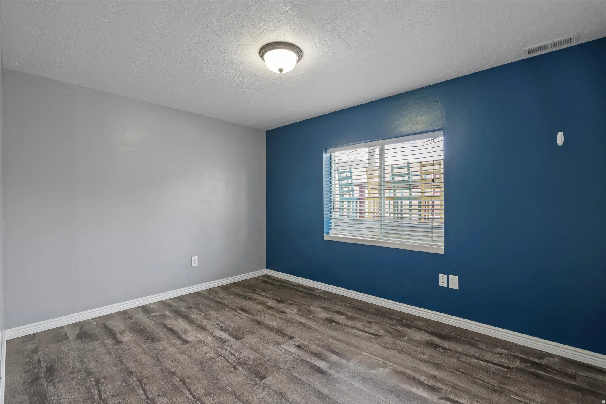 Room featuring a window with horizontal blinds, wood-finish flooring, and a flush mount ceiling light fixture