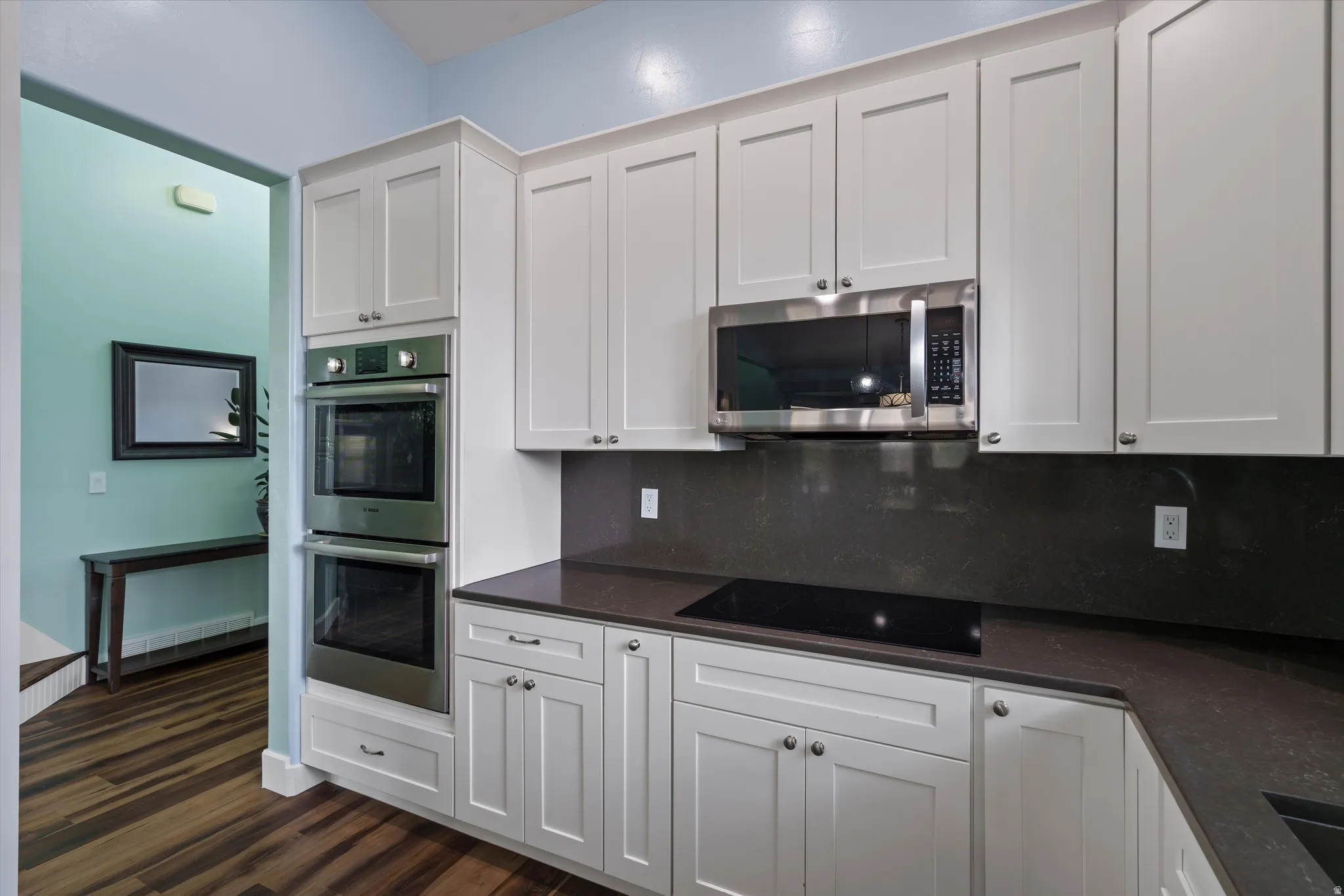 Modern kitchen featuring white shaker cabinetry, stainless steel double wall ovens, a built-in microwave, and a black cooktop