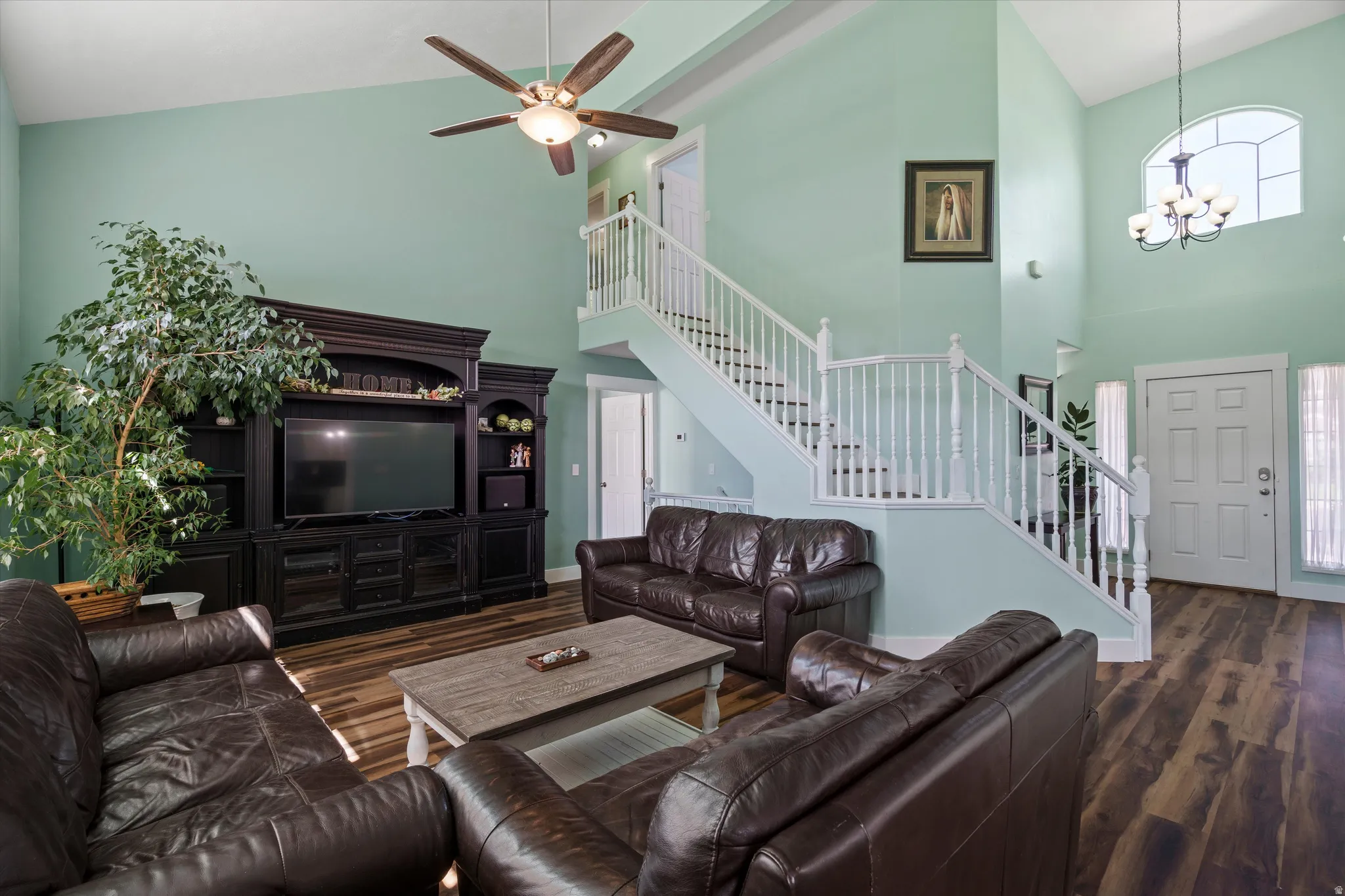 Two-story living area featuring vaulted ceilings, wood-finish flooring, and a prominent staircase with white railings