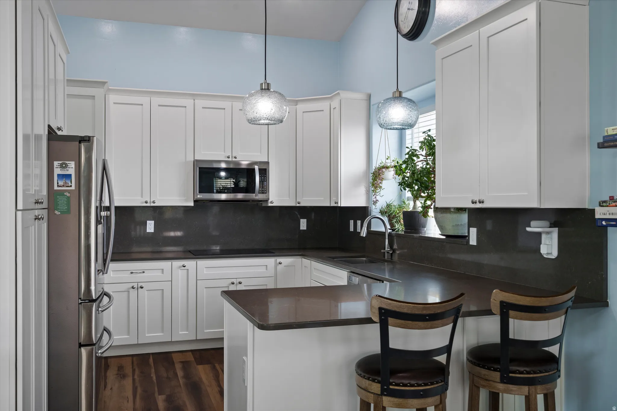 U-shaped kitchen featuring white cabinetry, dark countertops, wood-finish flooring, stainless steel appliances, and pendant lighting