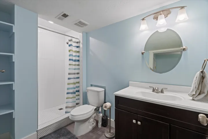 Bathroom featuring a single vanity with dark wood cabinetry, an integrated sink, and a circular mirror