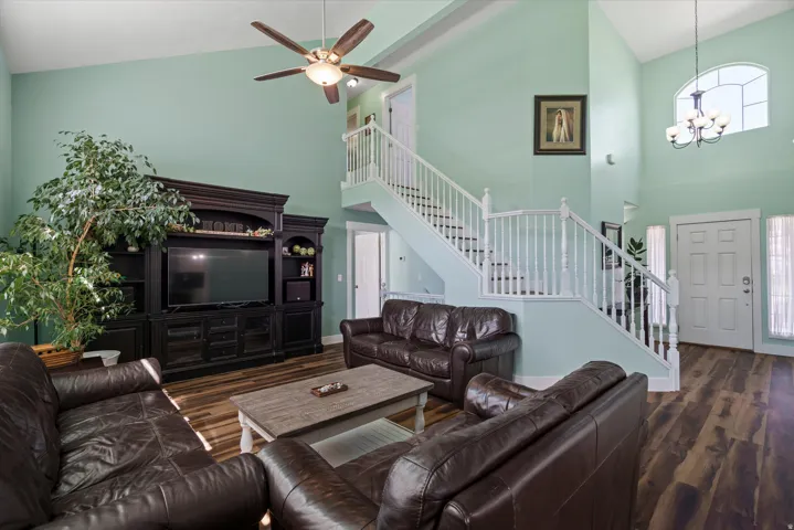 Two-story living area featuring vaulted ceilings, wood-finish flooring, and a prominent staircase with white railings