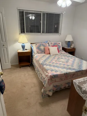 Carpeted room featuring a ceiling fan with light fixture and horizontal blinds on a window
