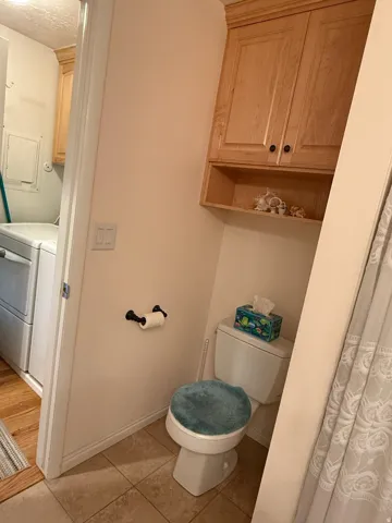 Recessed toilet area featuring overhead cabinetry with display shelving and tiled flooring