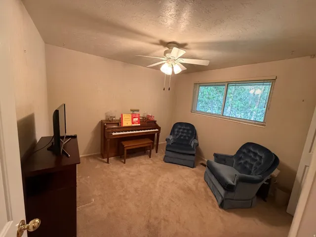 Carpeted room with a ceiling fan light fixture and a window with blinds