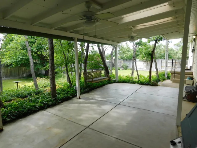 Covered patio with a concrete slab, exposed beam ceiling, and two ceiling fans