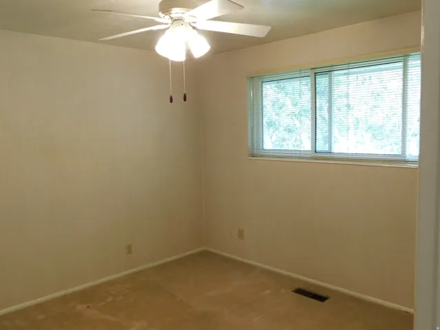 Carpeted room featuring a ceiling fan with integrated lighting, a window with horizontal blinds, and baseboard trim