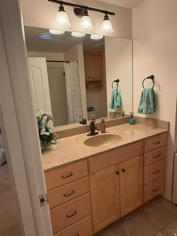 Vanity featuring a light-toned countertop with integrated sink, wood-finish cabinetry, and dark-finished hardware