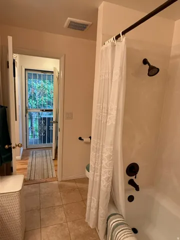 Bathroom featuring a white tub, dark bronze shower fixtures, and light-toned tile flooring