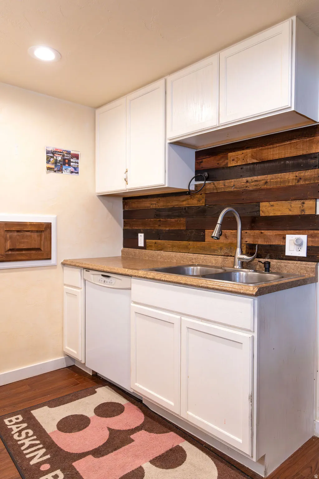 Kitchenette featuring a double basin stainless steel sink, white cabinetry, wood-finish flooring, a light-colored countertop, and a wood plank backsplash