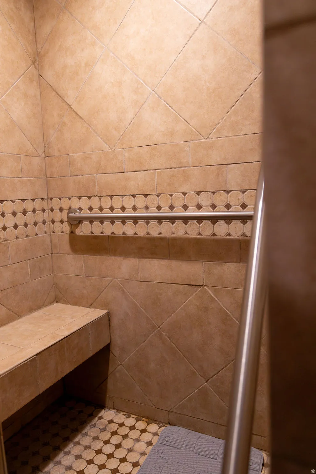 Tiled shower with a built-in bench, decorative accent tile band, and a metal grab bar