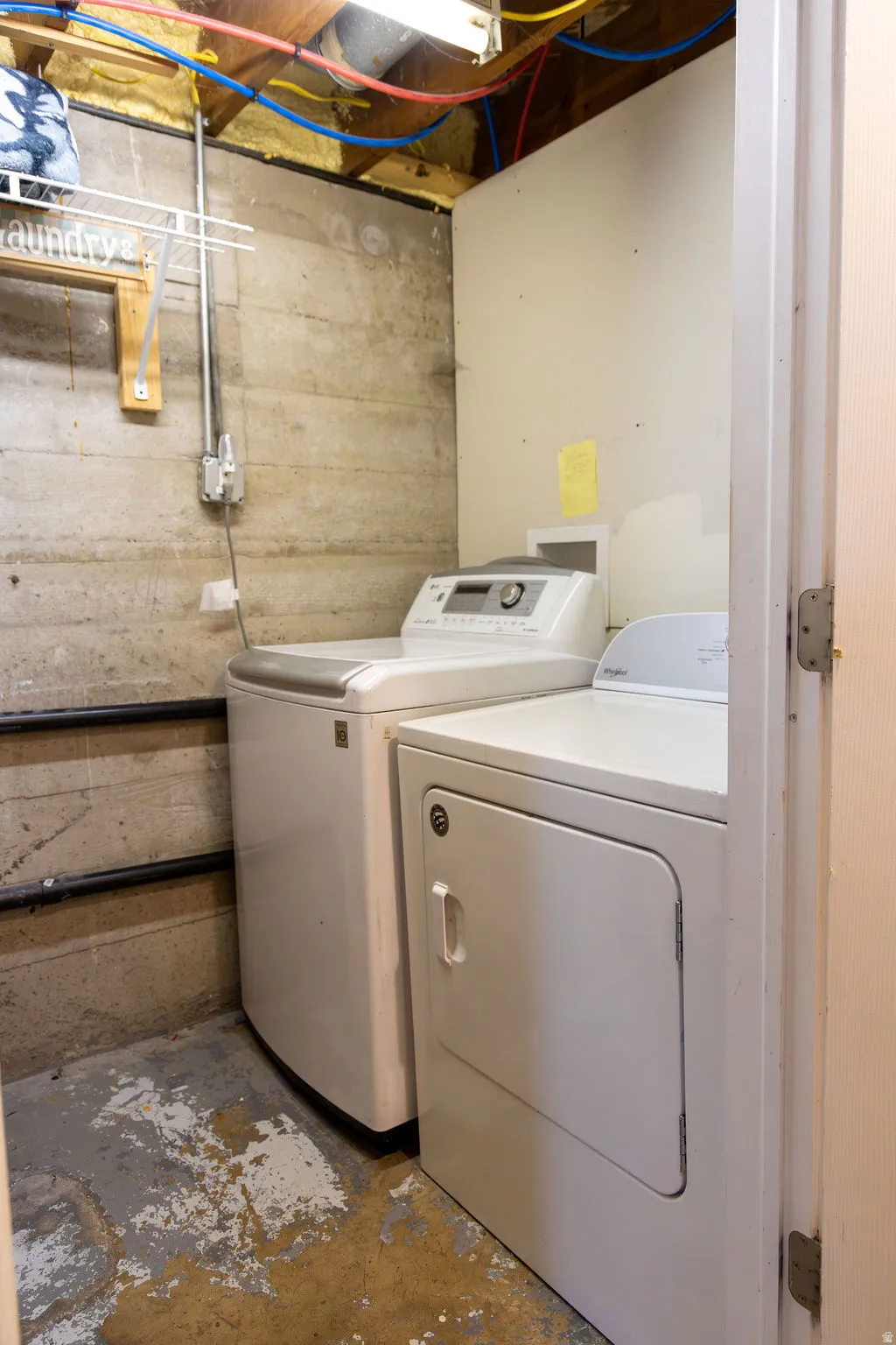 Dedicated laundry area featuring exposed concrete walls and ceiling joists
