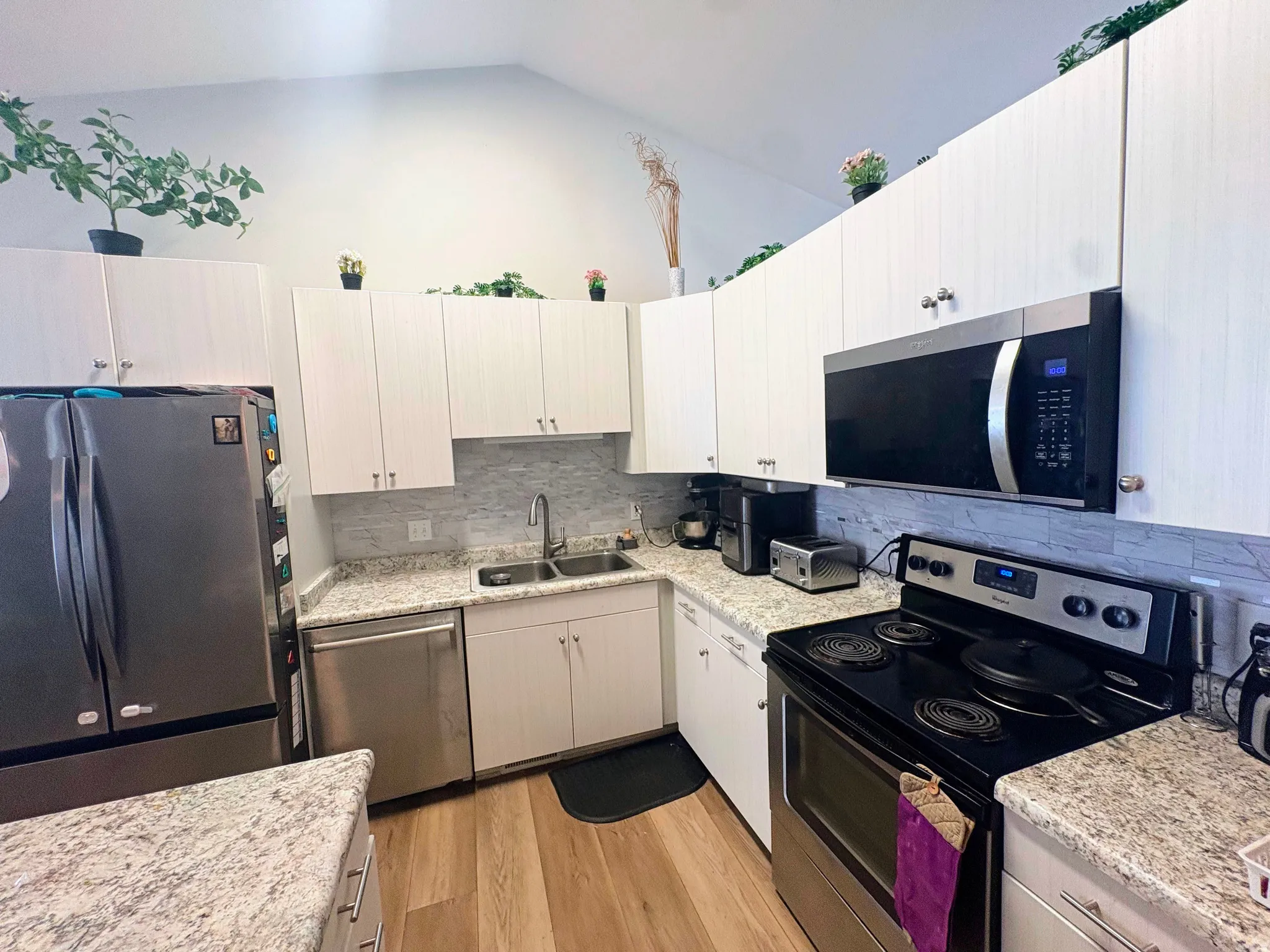 Modern kitchen featuring vaulted ceilings, light wood-finish flooring, white cabinetry, granite-style countertops, and stainless steel appliances