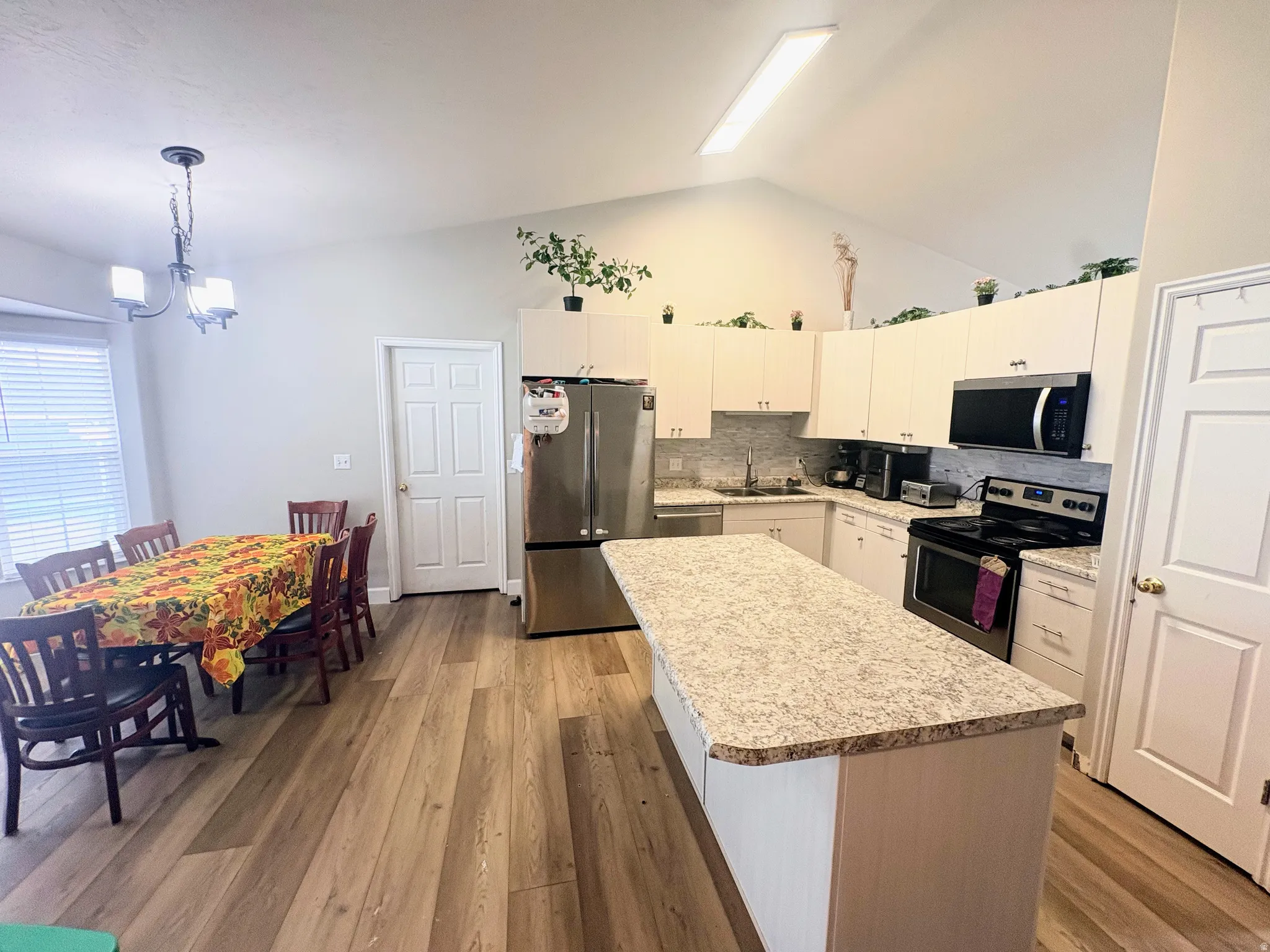 Kitchen featuring a vaulted ceiling with a linear light fixture, wood-finish flooring, a central island with a speckled countertop, white cabinetry, and stainless steel appliances