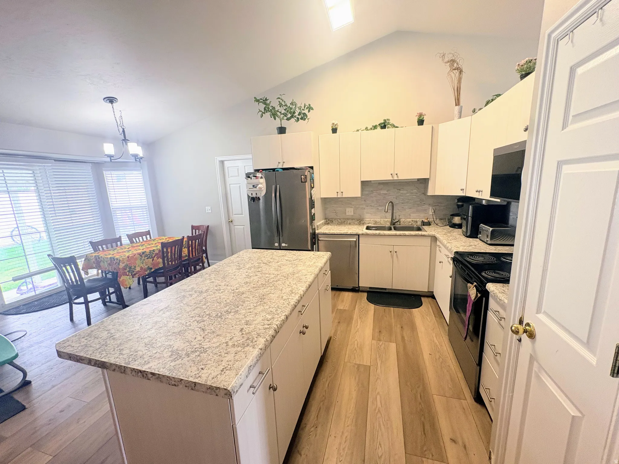 Vaulted ceiling kitchen featuring an island with a light-toned countertop, wood-finish flooring, white cabinetry, and stainless steel appliances