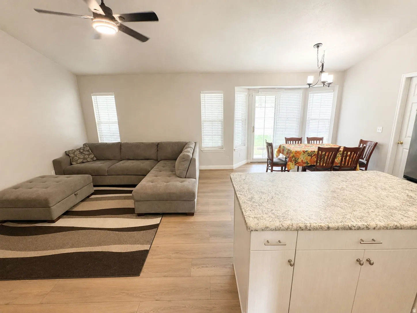 Open-concept interior featuring wood-finish flooring, a kitchen island with a light-colored countertop, and a dining area with bay windows