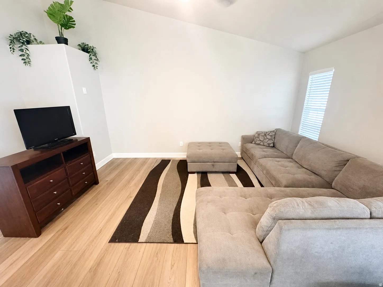 Expansive living area with light wood-finish flooring, vaulted ceilings, and a corner window with horizontal blinds