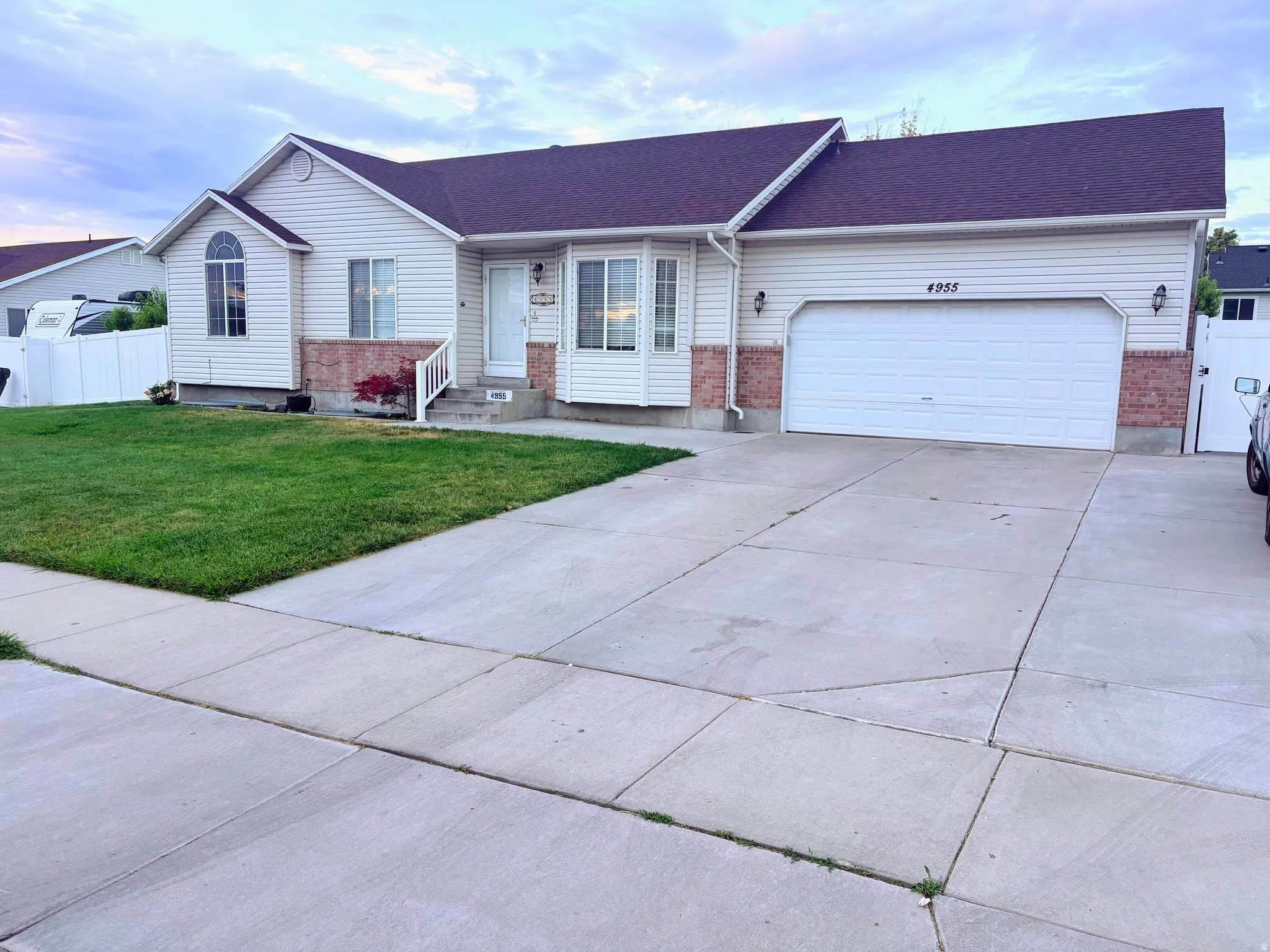 White vinyl siding exterior with brick accents, dark shingle roof, arched accent window, concrete driveway, and attached two-car garage