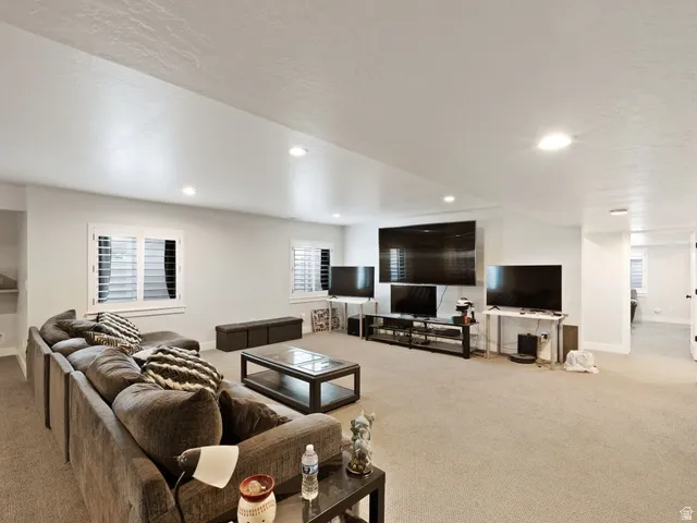 Spacious recreation room featuring recessed lighting, light-colored carpeting, two windows with plantation shutters, and light gray wall paint
