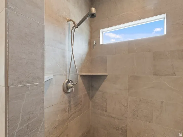 Tiled shower enclosure featuring a multi-function shower head with a handheld sprayer, an integrated soap niche, a corner shelf, and a horizontal transom window