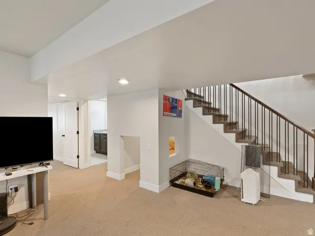 Carpeted lower level with recessed lighting, featuring a staircase with dark wood-finish handrail and black metal balusters