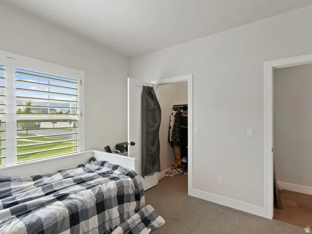 Bedroom featuring a large window with plantation shutters, neutral wall paint, and carpet flooring