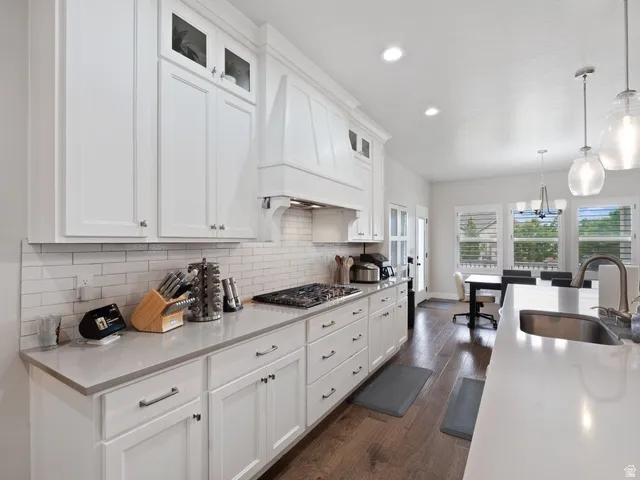 Open-concept kitchen featuring white shaker cabinetry, light-toned countertops, a subway tile backsplash, and dark wood-finish flooring