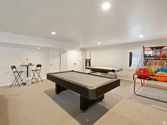 Carpeted recreation room featuring recessed lighting, a window with louvered shutters, and multiple white panel doors