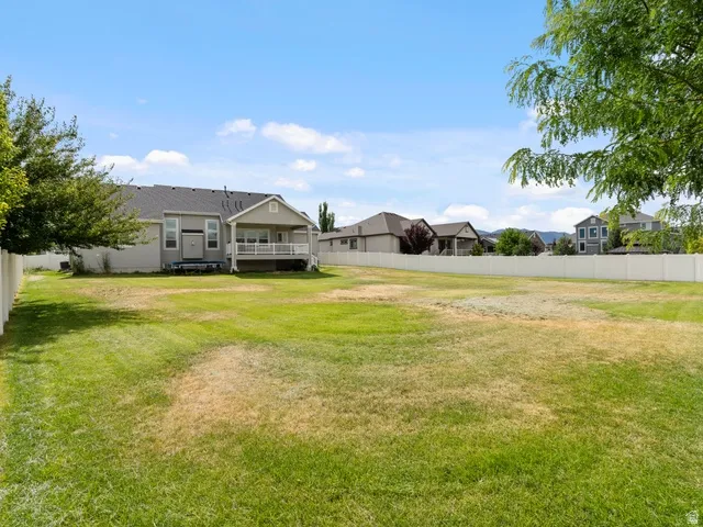 Expansive grassy yard area with a vinyl fence border, featuring a modern residence with a covered patio