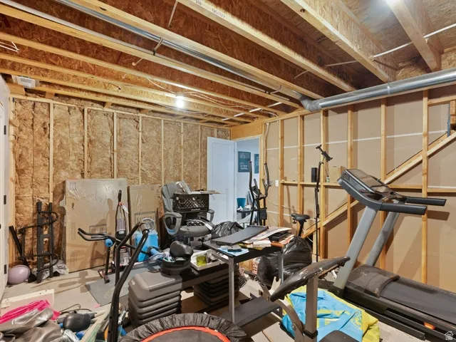Unfinished basement area featuring exposed wood joists, structural framing, visible insulation, and a white interior door