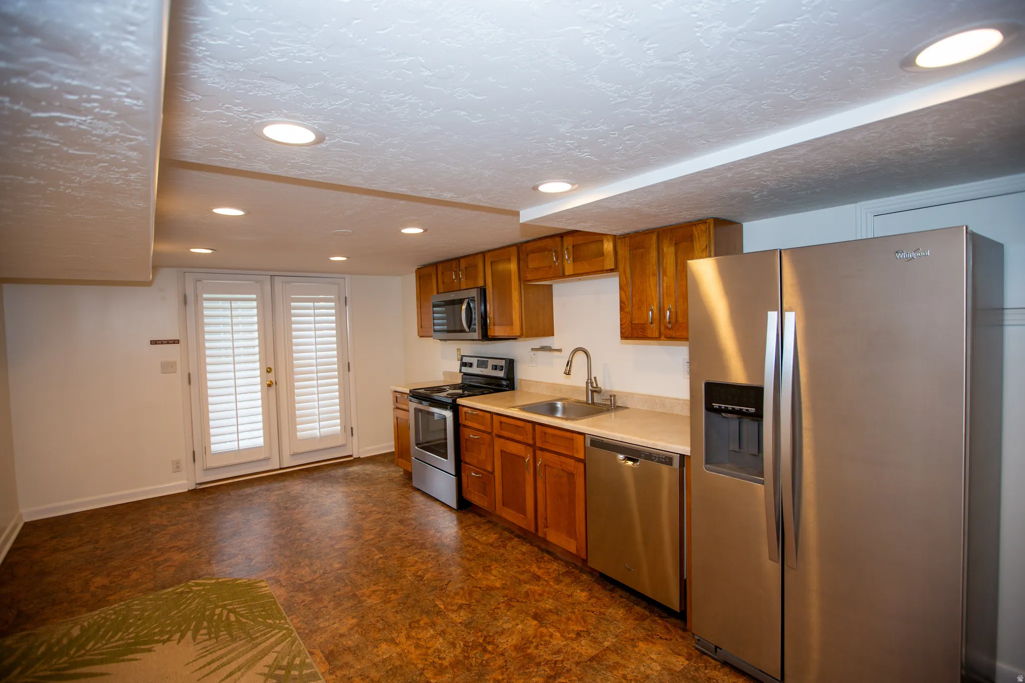 Basement kitchen featuring wood cabinetry, stainless steel appliances, and a double basin sink