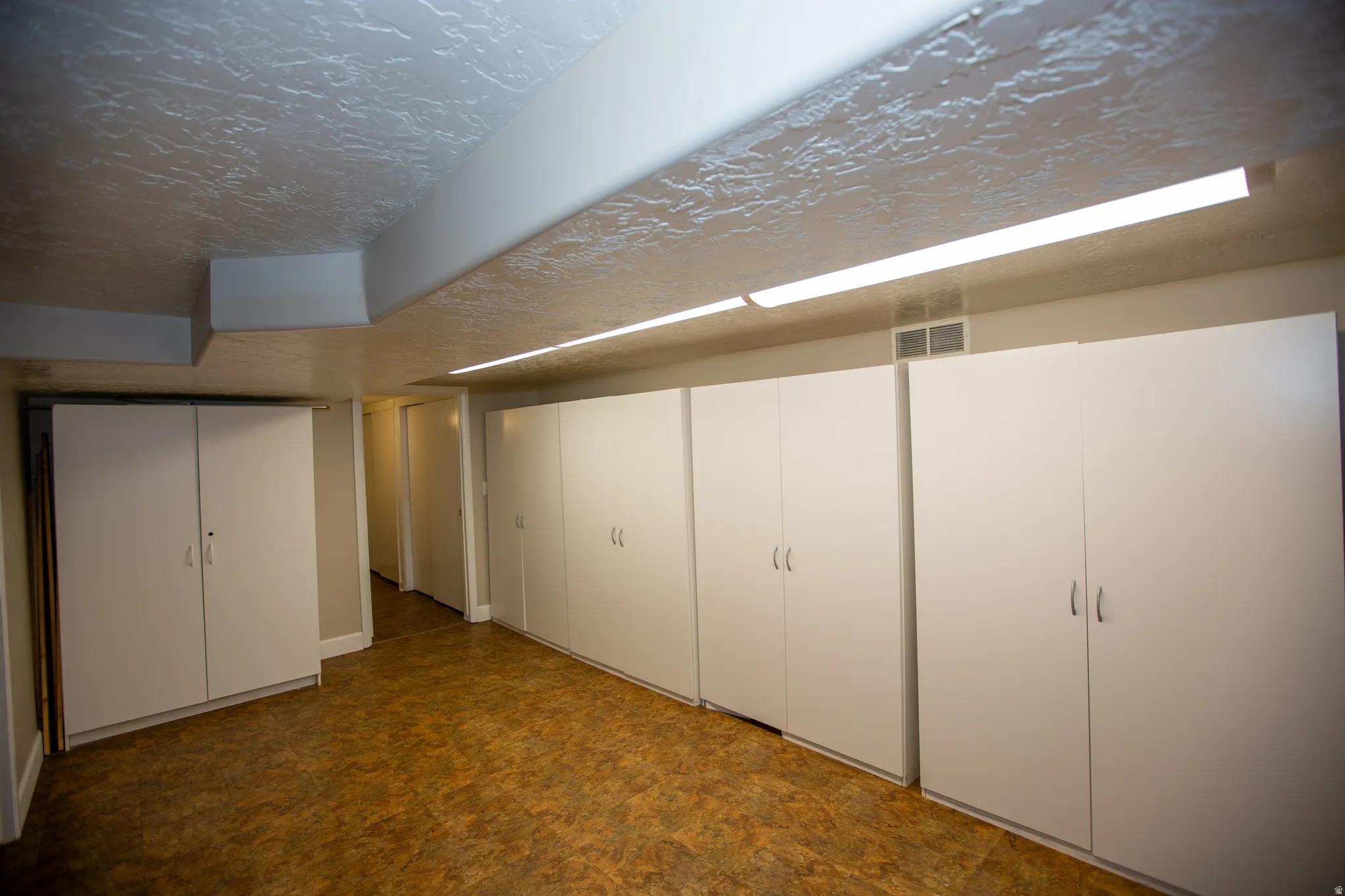 Extensive white cabinetry providing ample storage, textured ceiling, fluorescent strip lighting, and durable flooring