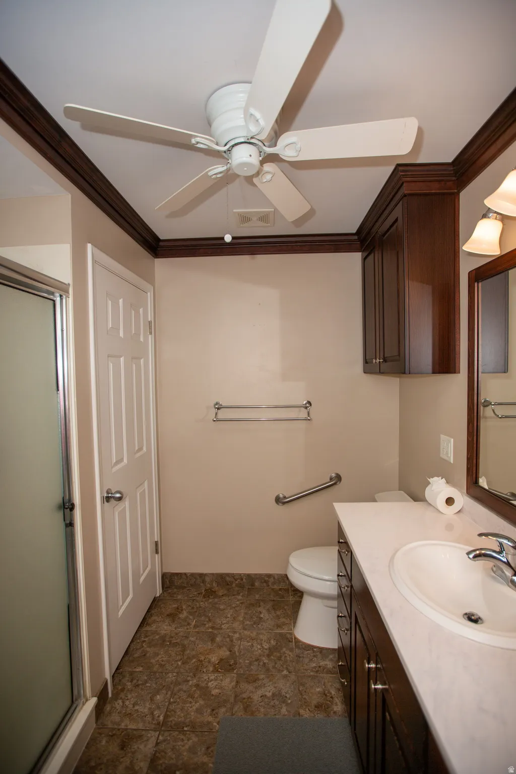 Bathroom featuring a shower enclosure with frosted glass, a vanity with a white countertop and integrated sink, a dark wood-finish vanity cabinet, a wall-mounted light fixture, and a ceiling fan
