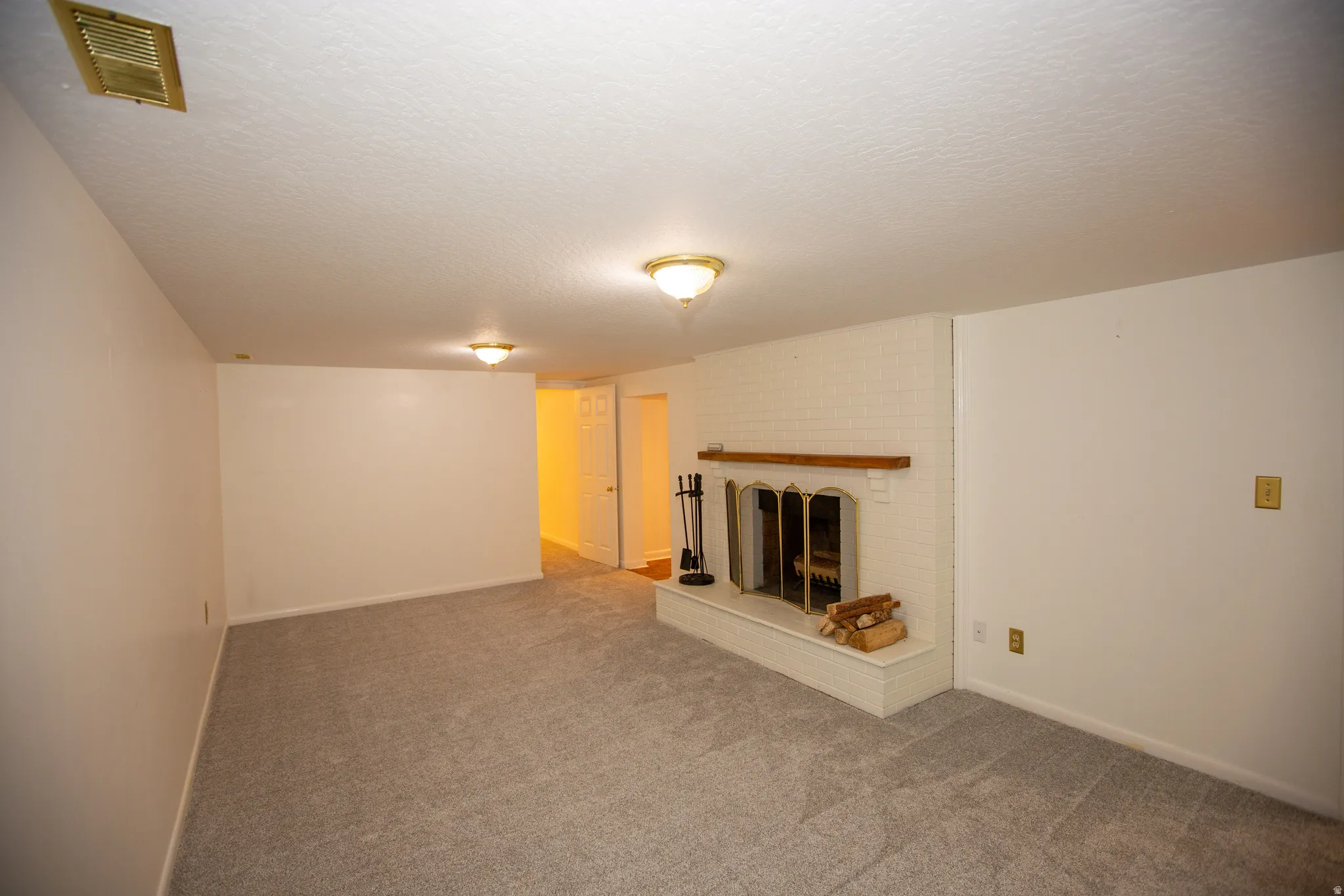 Carpeted room featuring a white brick fireplace with a wood mantle, a firebox with a metal screen, and a hearth