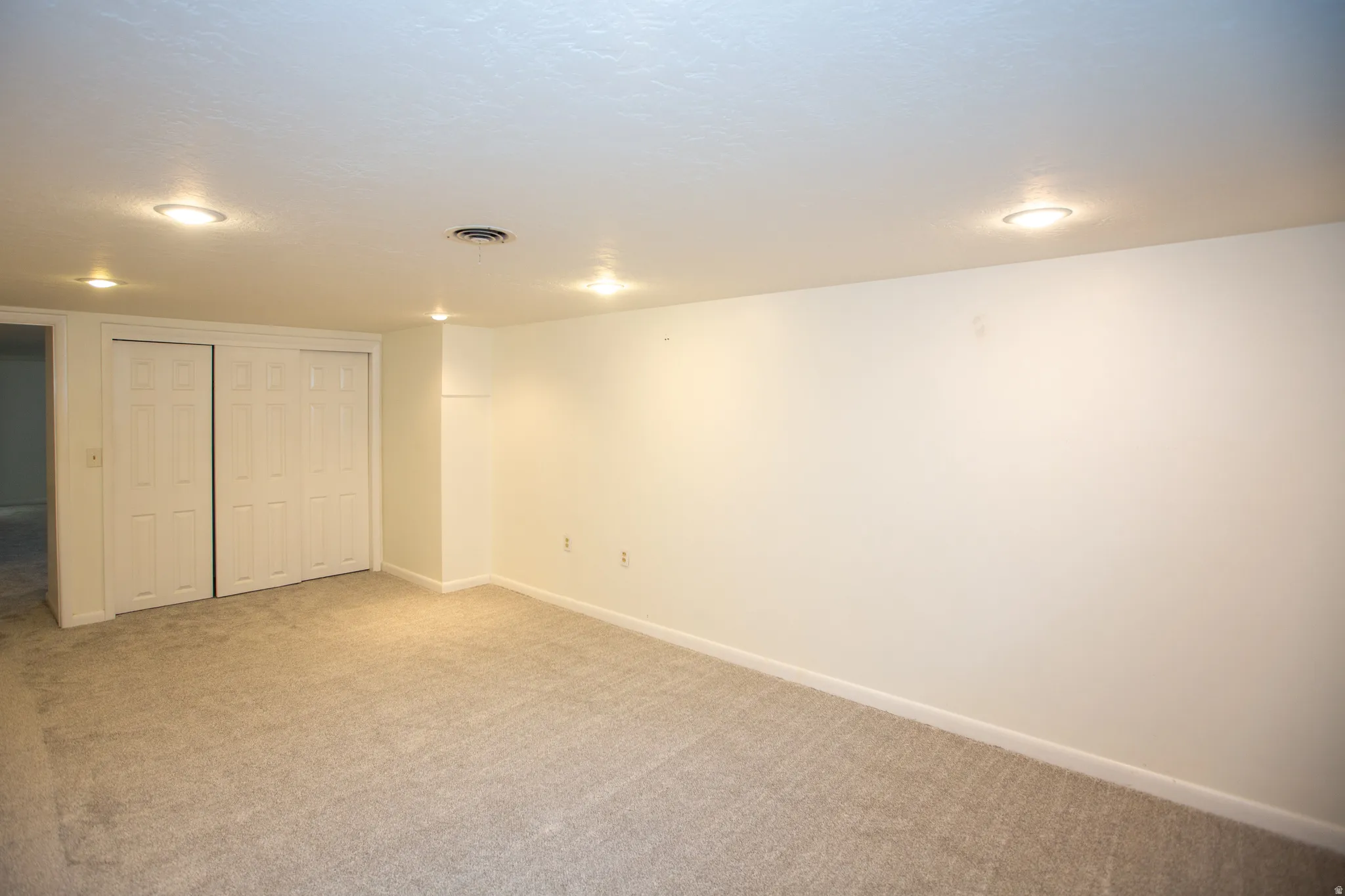 Spacious room featuring neutral carpet flooring, white walls, recessed ceiling lighting, and bi-fold closet doors