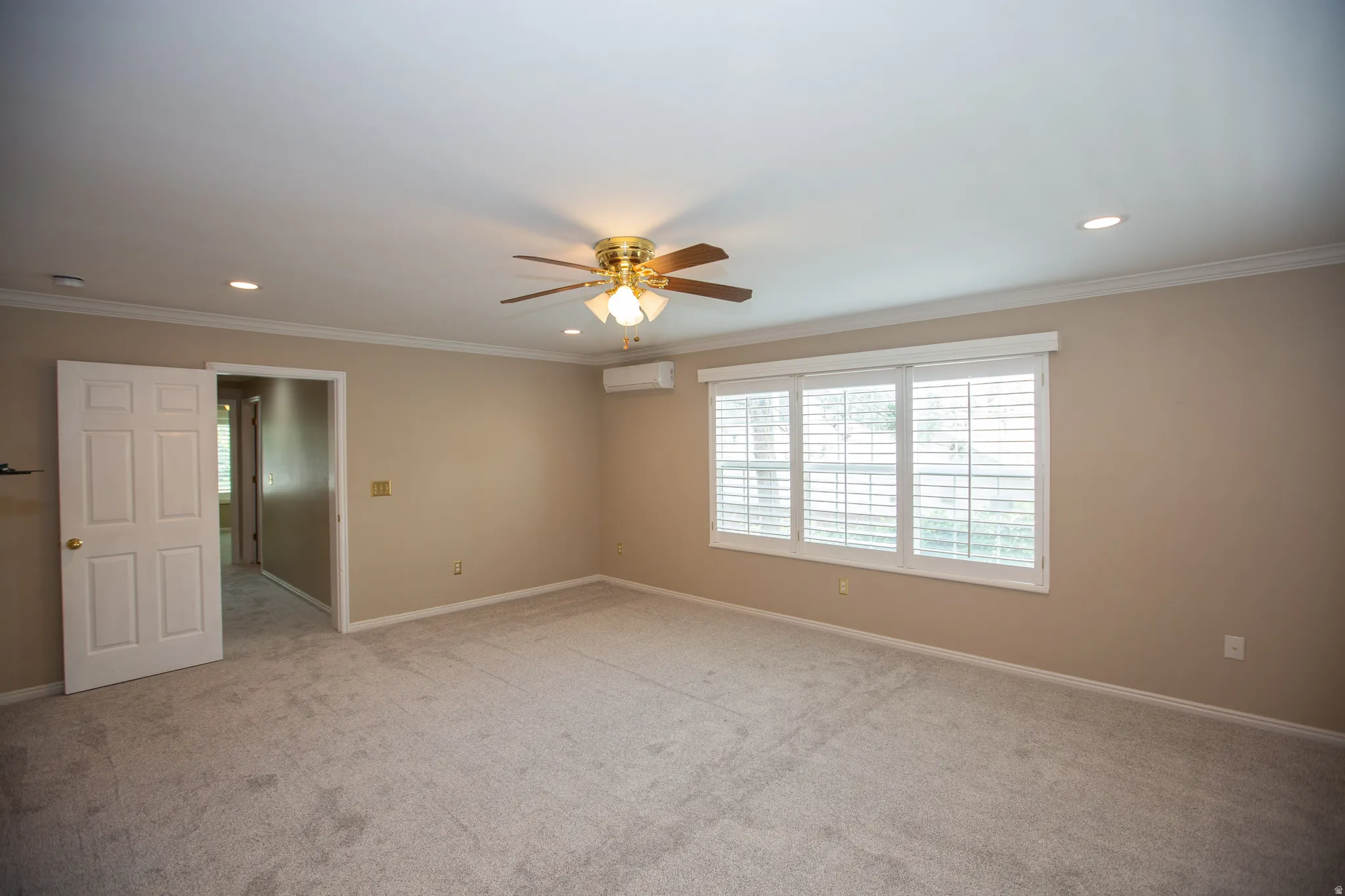 Spacious primary bedroom featuring neutral carpeting, light beige walls, and white crown molding