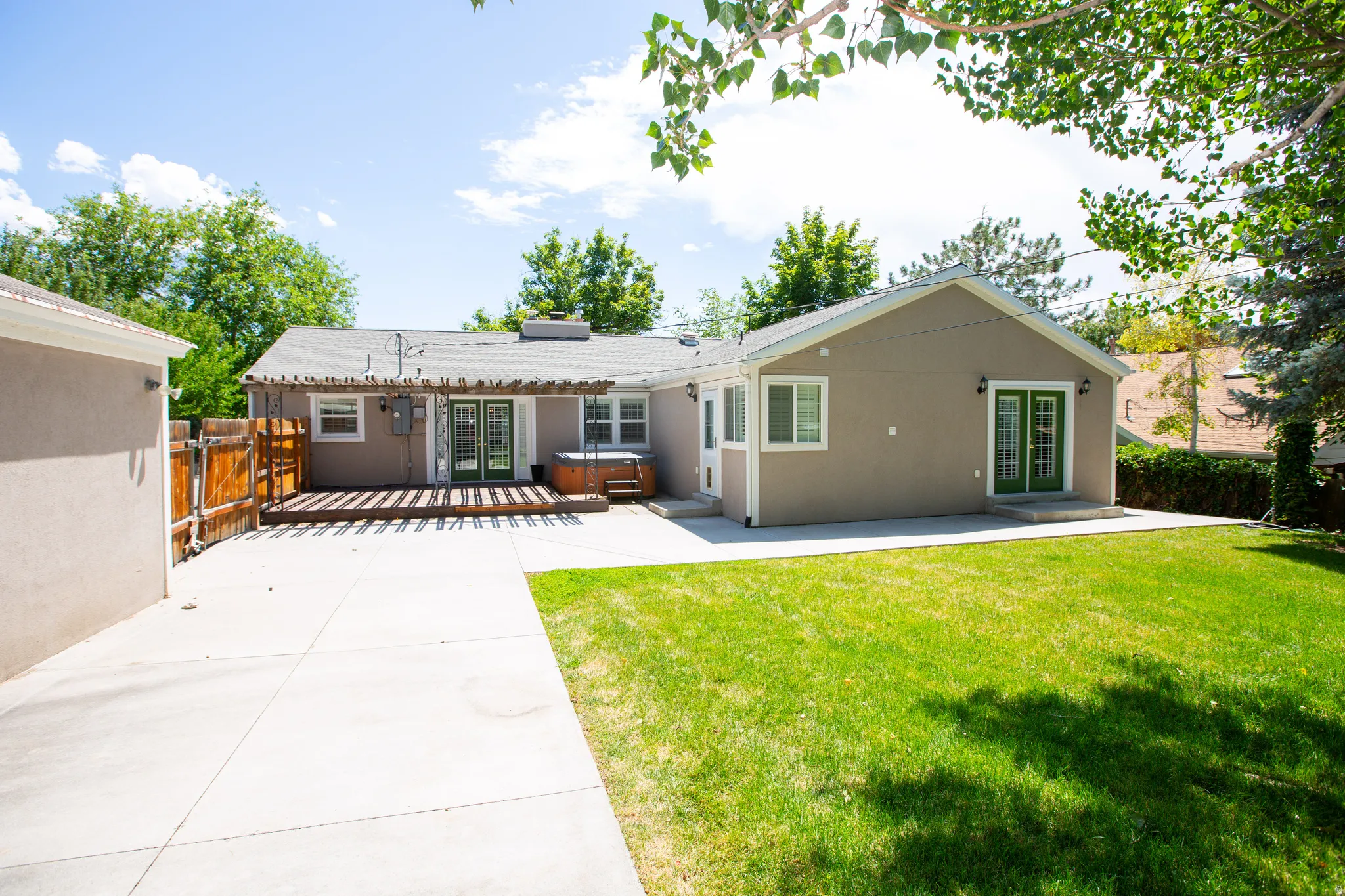 Rear exterior featuring a large concrete patio, expansive lawn, and wooden deck with a pergola