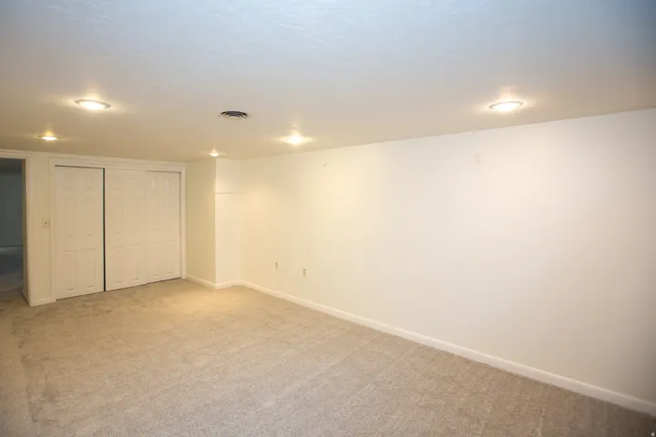 Spacious room featuring neutral carpet flooring, white walls, recessed ceiling lighting, and bi-fold closet doors