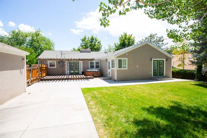 Rear exterior featuring a large concrete patio, expansive lawn, and wooden deck with a pergola