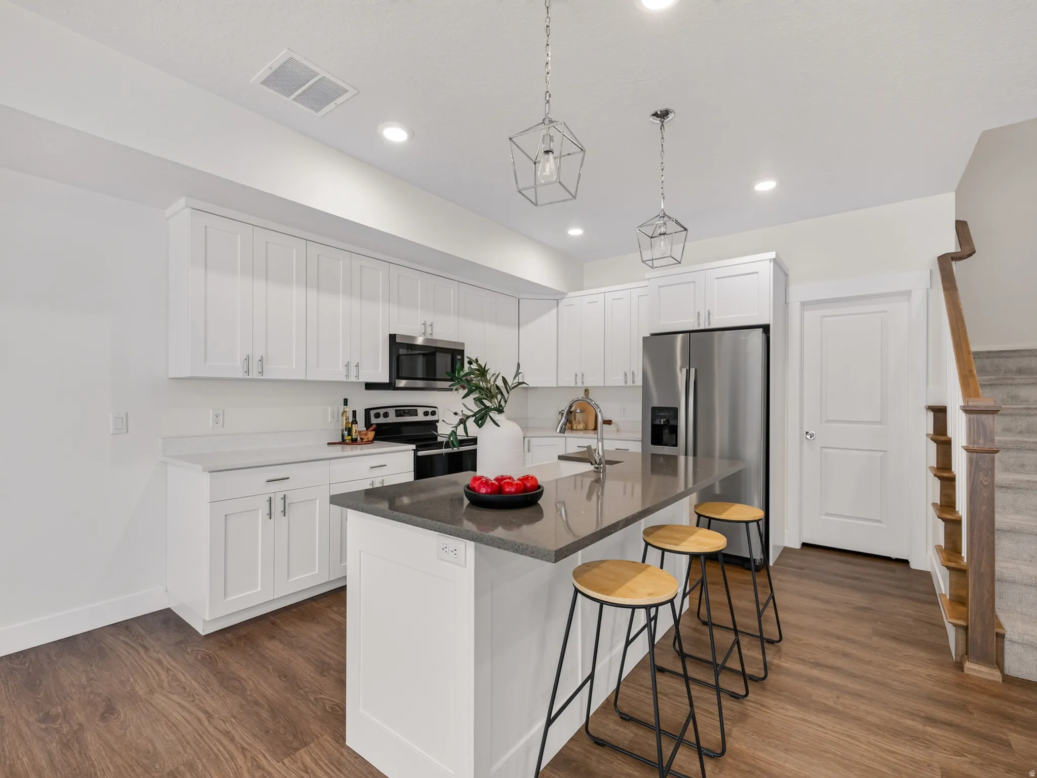 Modern kitchen featuring white shaker cabinetry, stainless steel appliances, a center island with a stone countertop, and wood-finish flooring