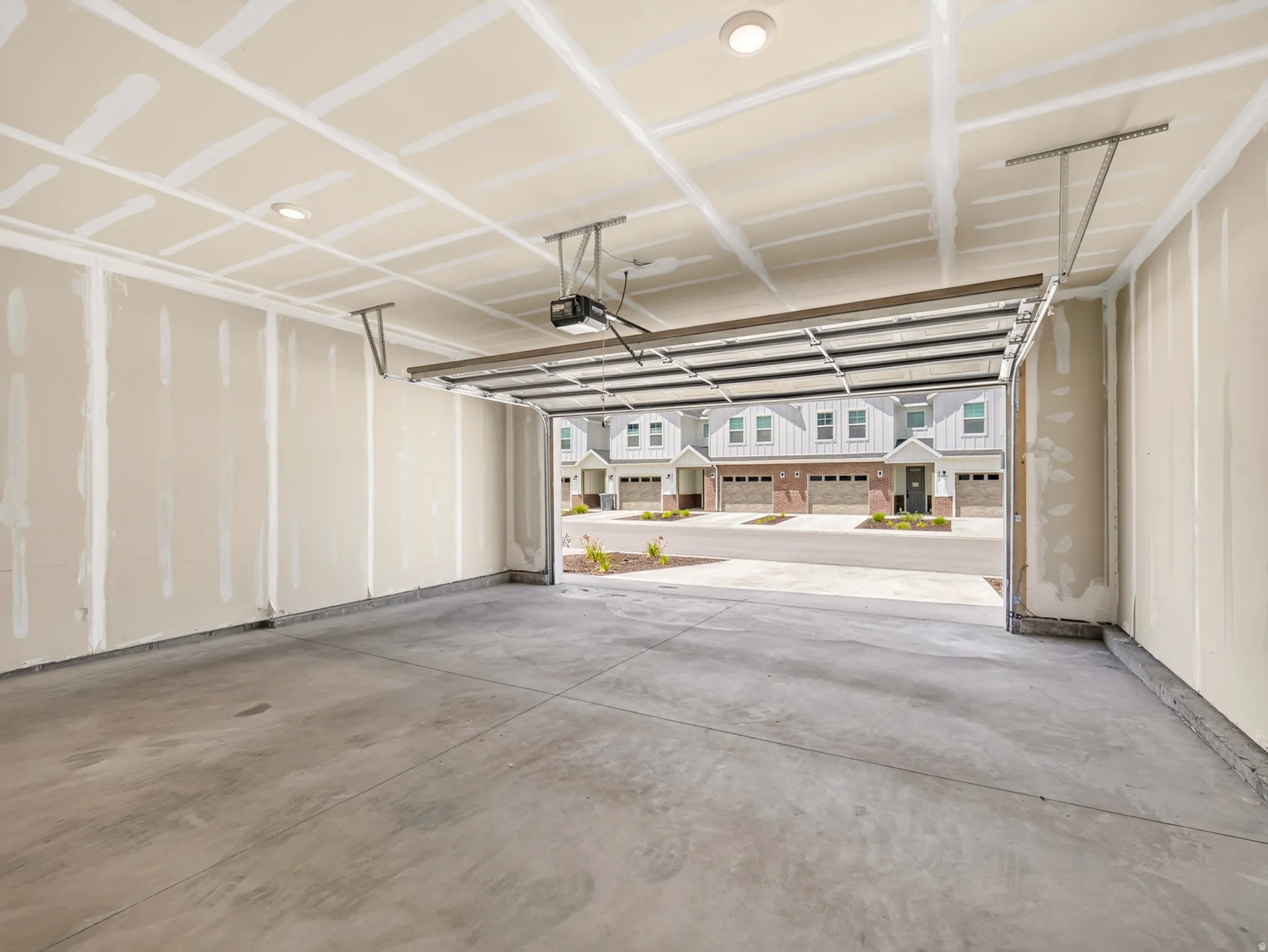 Spacious garage featuring a concrete floor, exposed drywall walls, recessed ceiling lighting, and an overhead garage door opener
