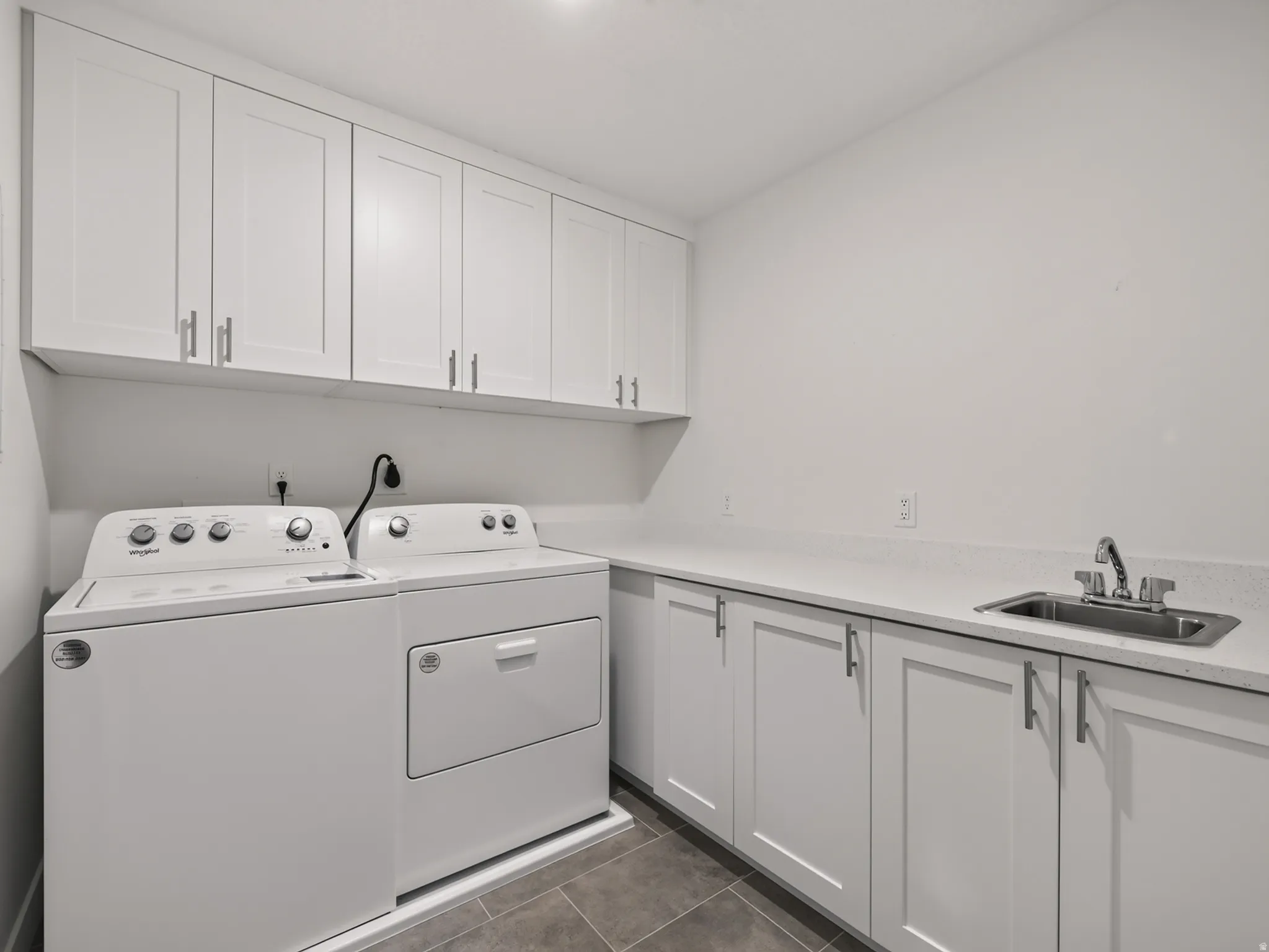 Utility room featuring white shaker-style cabinetry with brushed nickel hardware, light-toned countertops, and a stainless steel sink with a chrome faucet