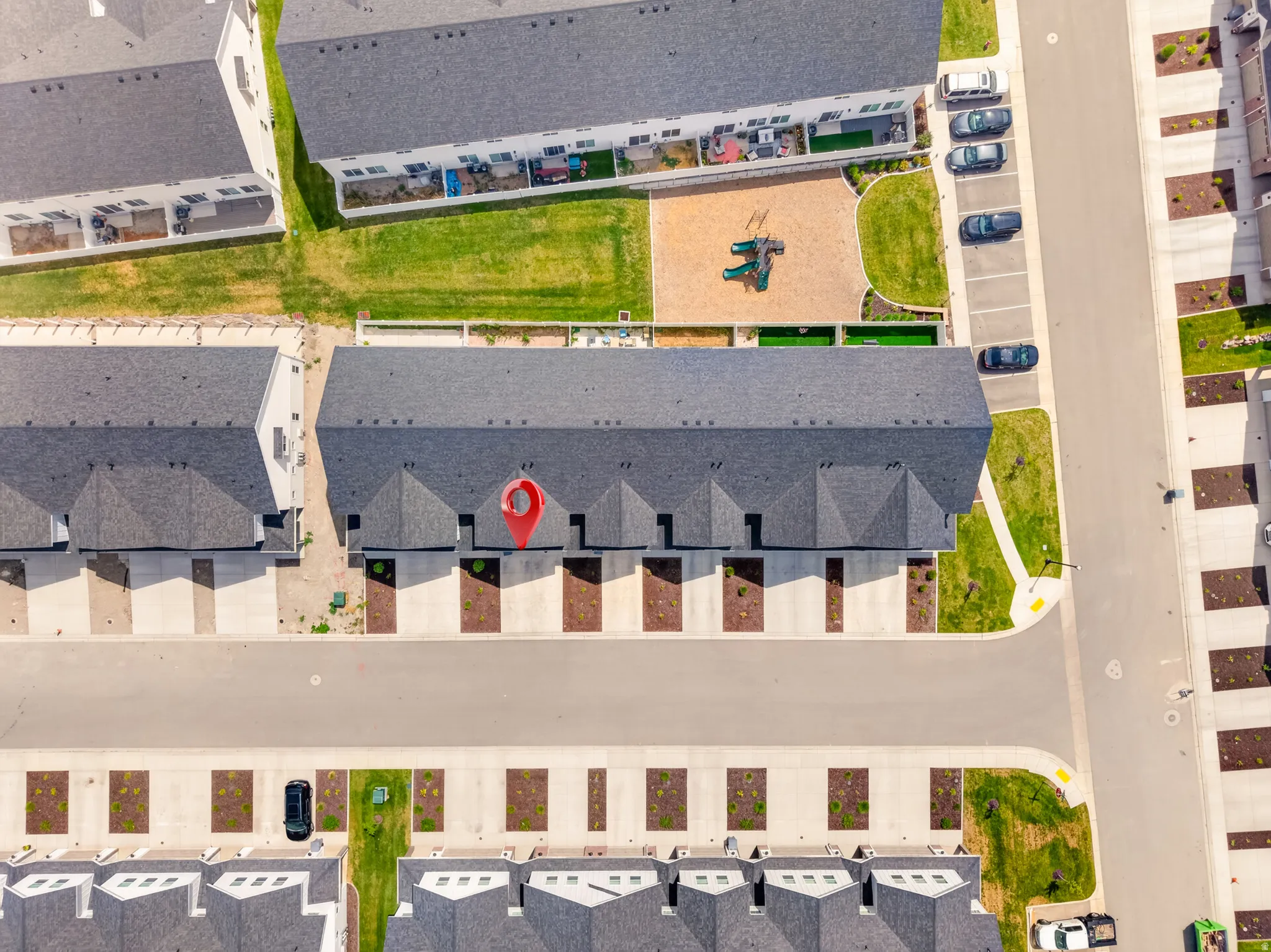 Contemporary townhome property featuring a dark gray shingle roof, paved driveway, and dedicated landscaping