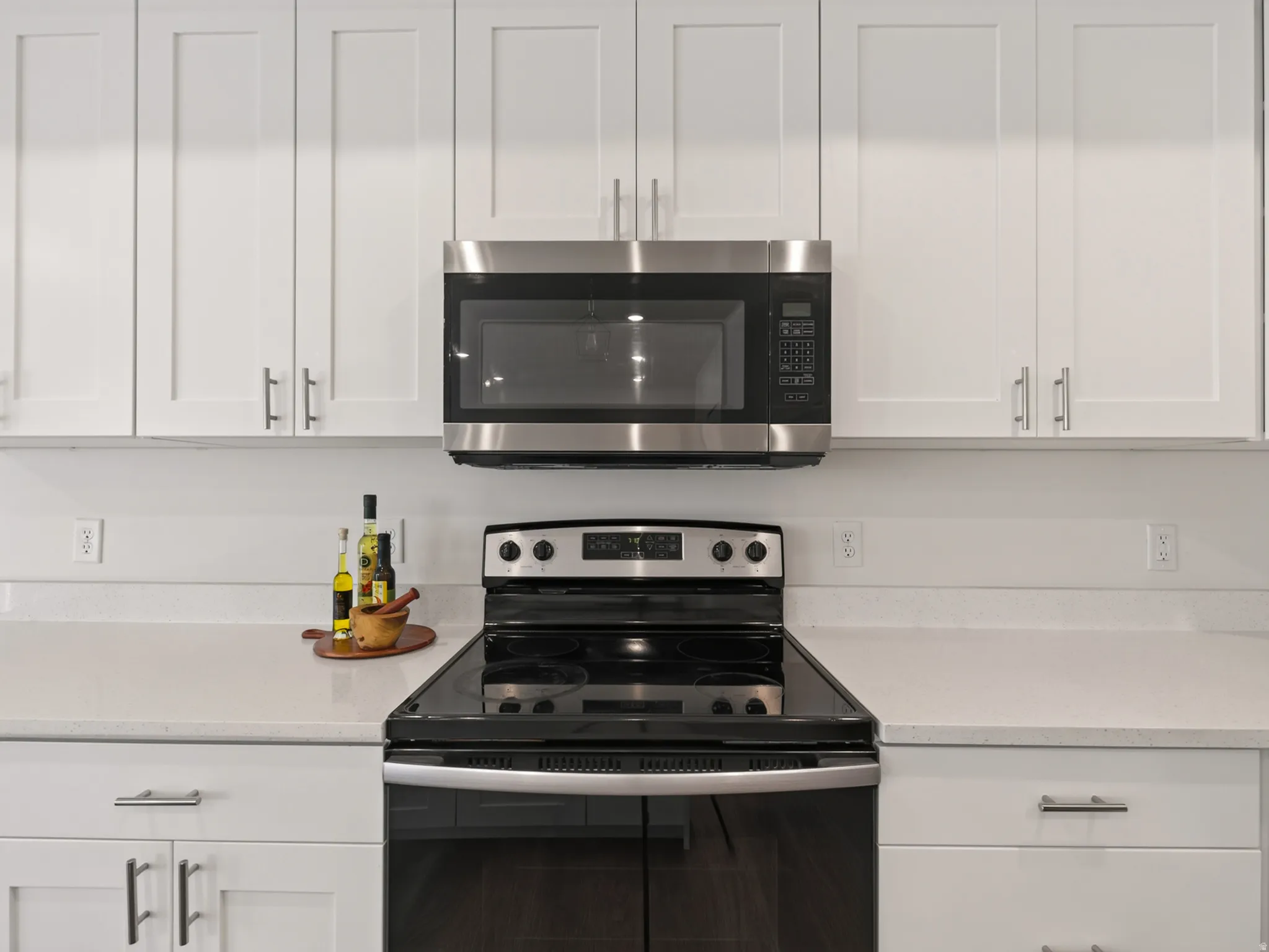 Modern kitchen featuring white shaker cabinetry, stainless steel microwave, black electric range, and light-toned countertops