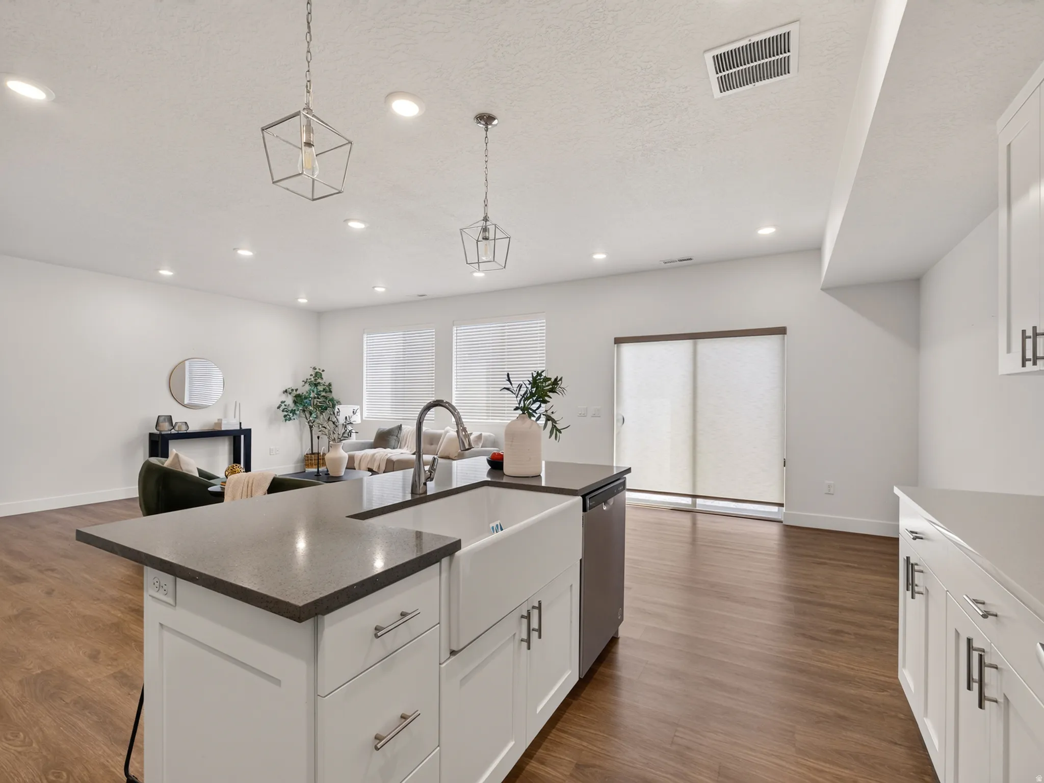 Kitchen island featuring a farmhouse sink, dark countertop, and white cabinetry