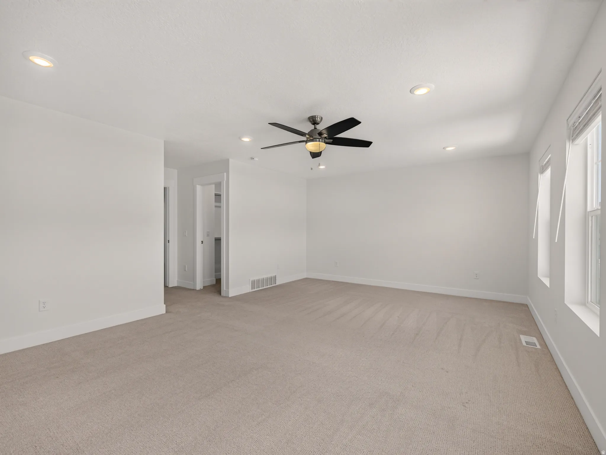 Spacious room featuring neutral carpeting, white walls, recessed lighting, and a ceiling fan