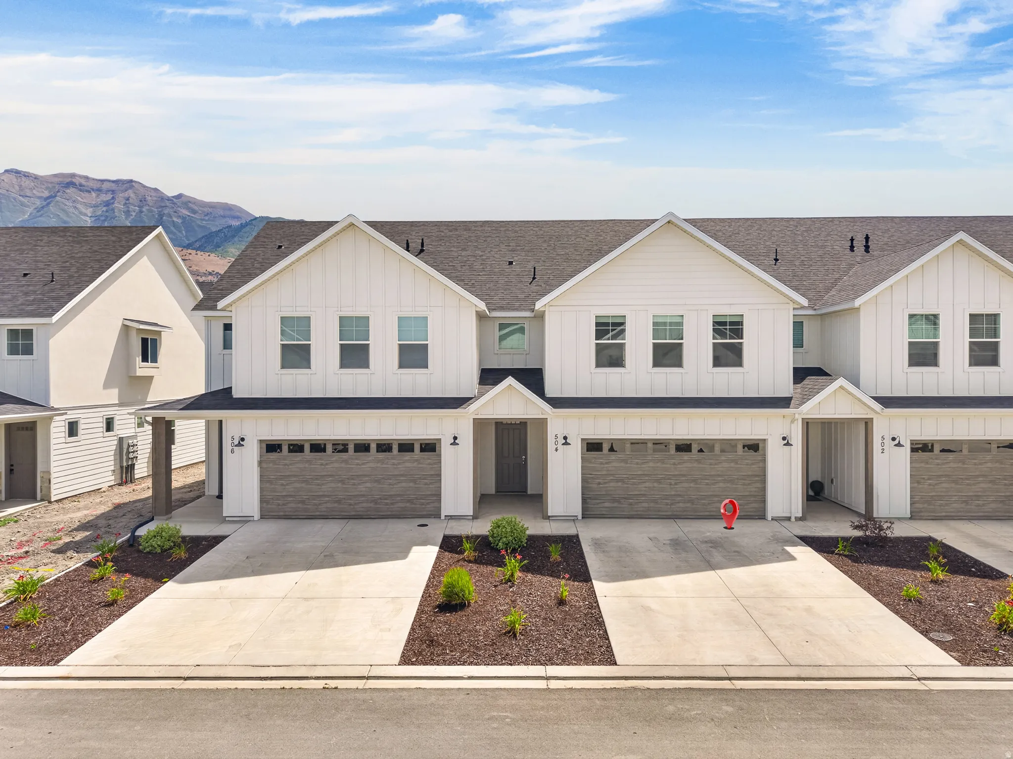 Modern farmhouse-style townhome featuring white vertical siding, dark gray roofing, and a two-car garage with a wood-look door
