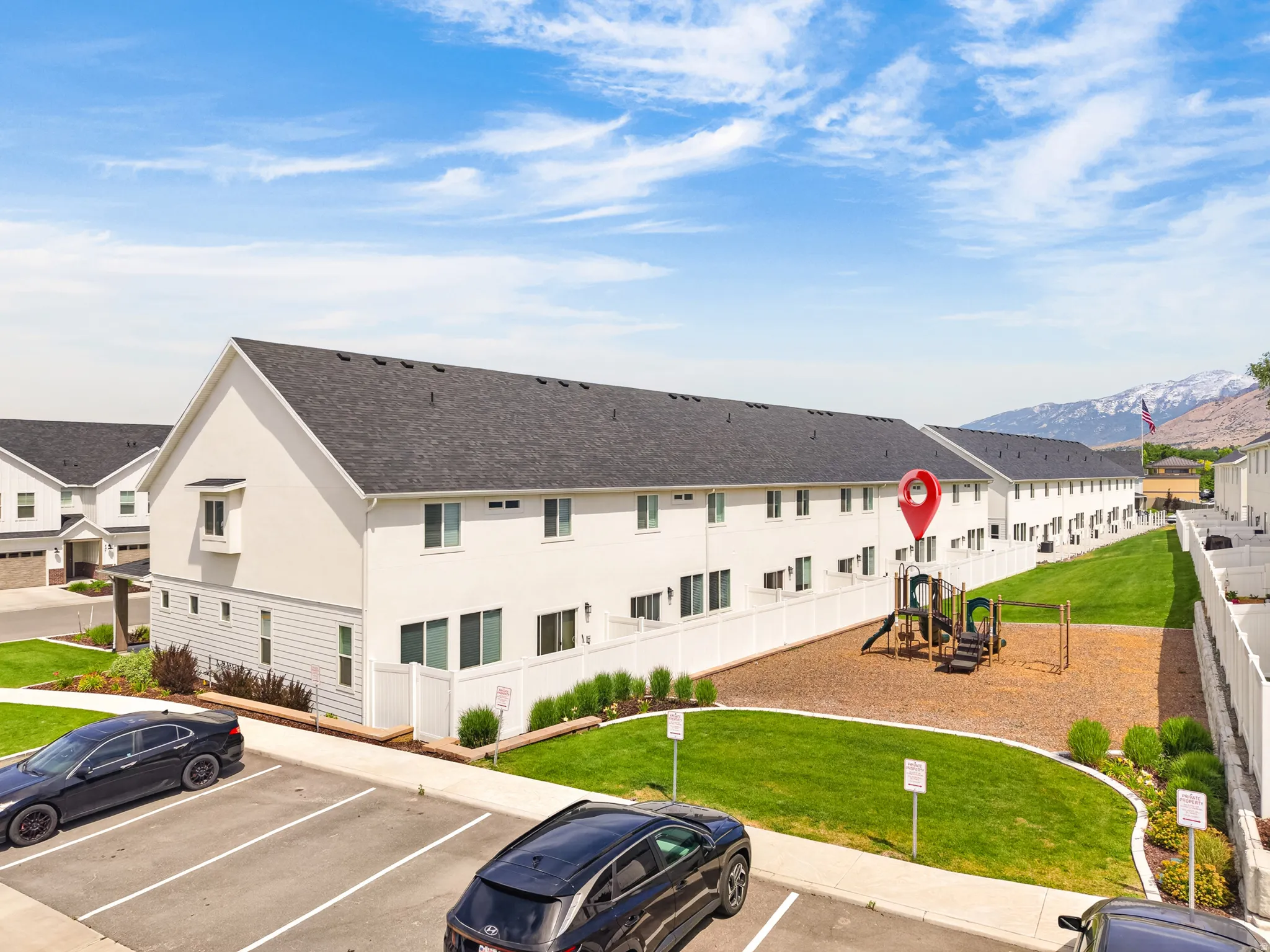 Townhome community featuring white exteriors, dark shingle roofs, and a children's play area with wood chip ground cover