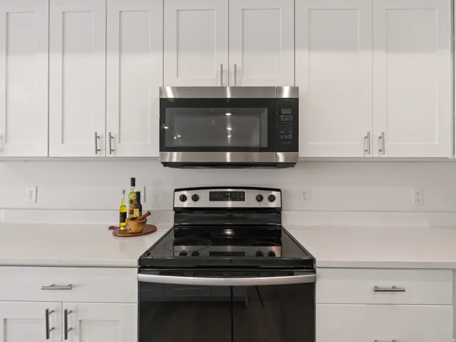Modern kitchen featuring white shaker cabinetry, stainless steel microwave, black electric range, and light-toned countertops